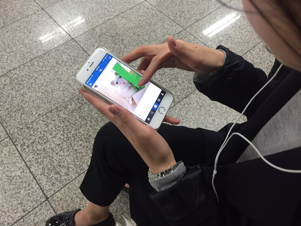 이어폰을 낀 사람이 두 손으로 스마트폰을 쥐고 화면을 손가락으로 넘기는 모습