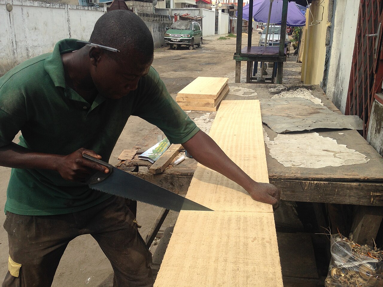 작업대 위에 놓인 넓은 나무판을 톱(수공구)으로 켜서 자르는 사람의 모습